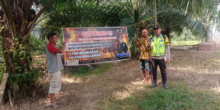 Anggota Polsek Belitang III memasang spanduk himbauan karhutla. (Foto/Yesi)
