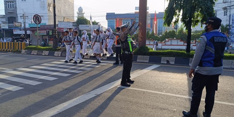 Personil Polres Langkat Bantu Penyeberangan Siswa Sekolah dan Urai Kemacetan. (Foto/Jhon).